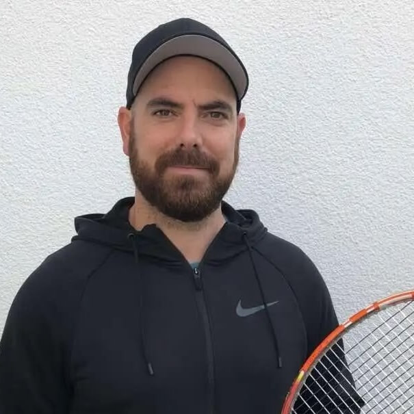 Mann mit Tennisschläger vor weißer Wand