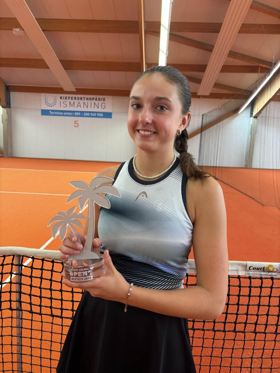 Tennisspielerin hält Pokal auf Hallenplatz