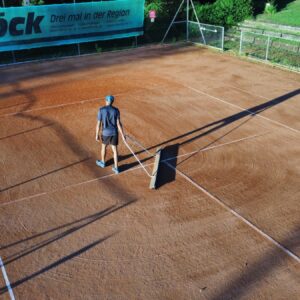 Person pflegt Tennisplatz mit Abziehnetz