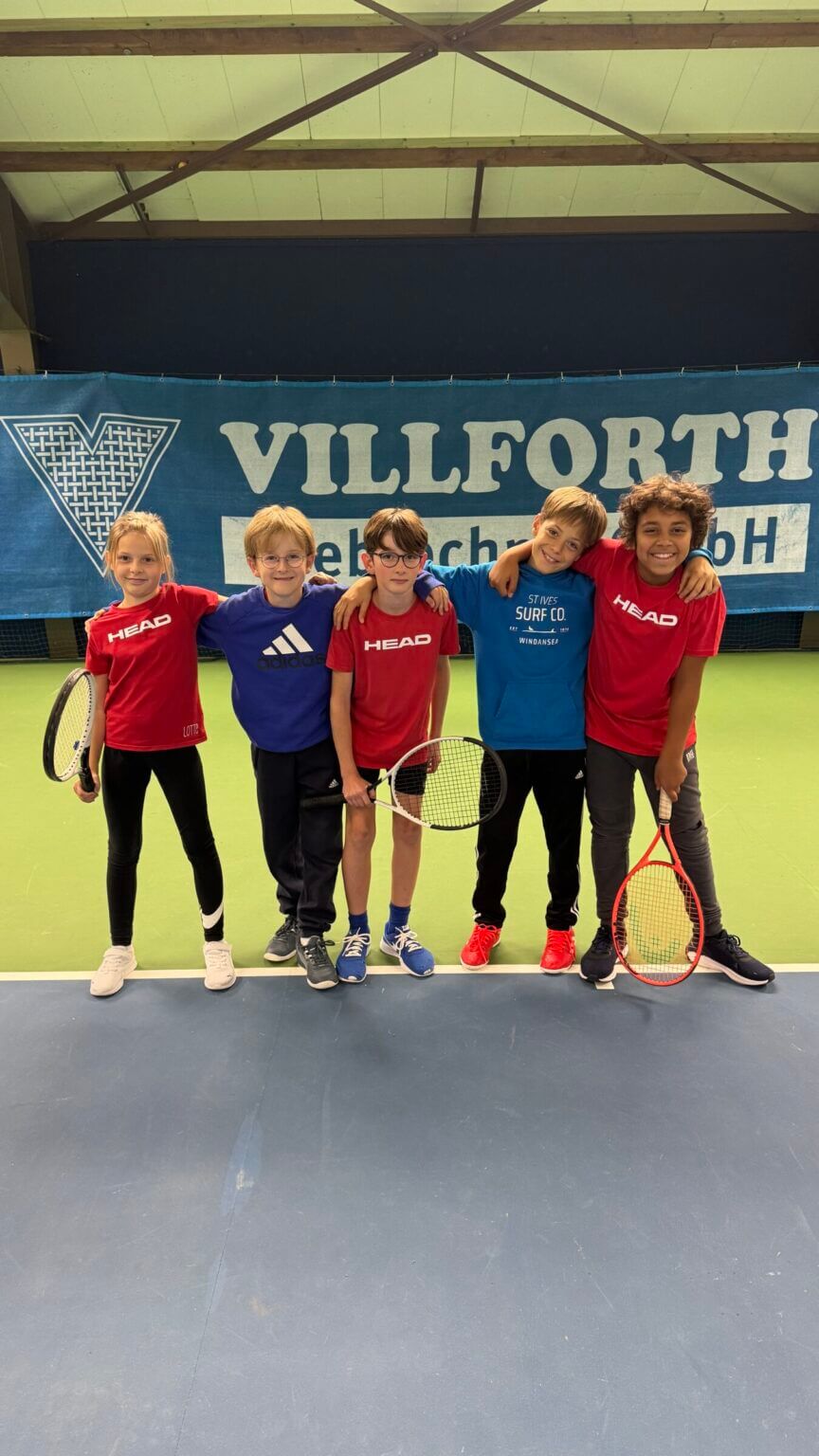 Kinder spielen Tennis in einer Sporthalle