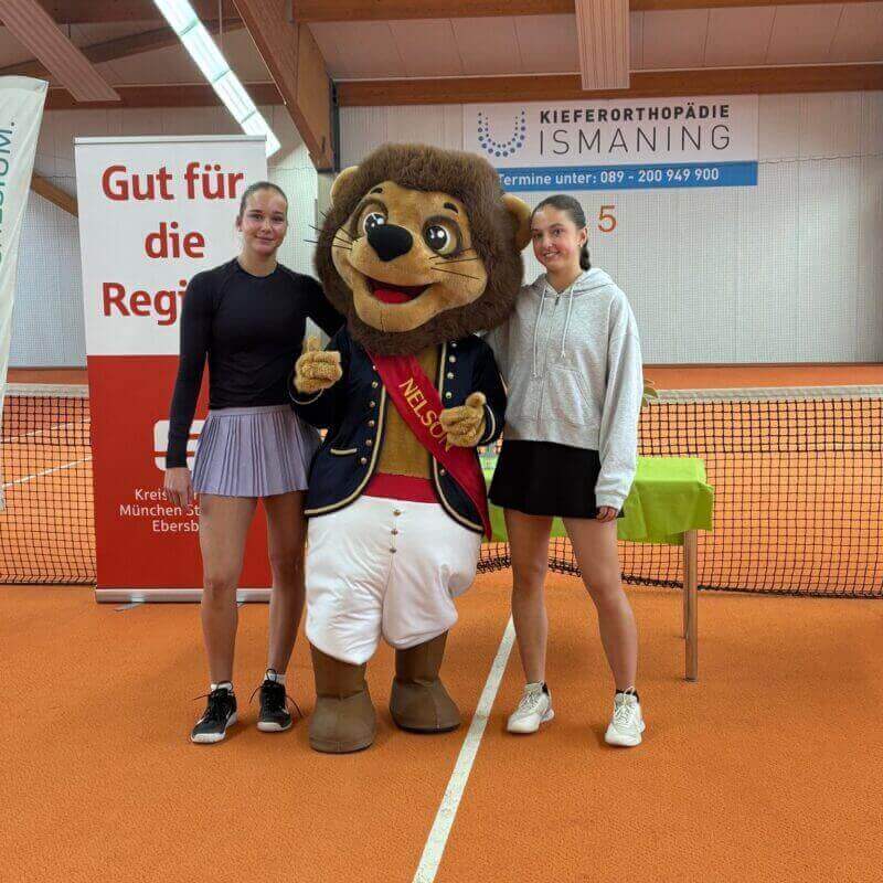 Zwei Tennisspielerinnen mit Löwenmaskottchen in Tennishalle