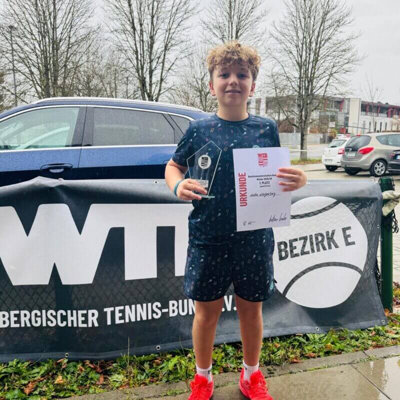 Junge mit Tennis-Urkunde und Pokal im Freien