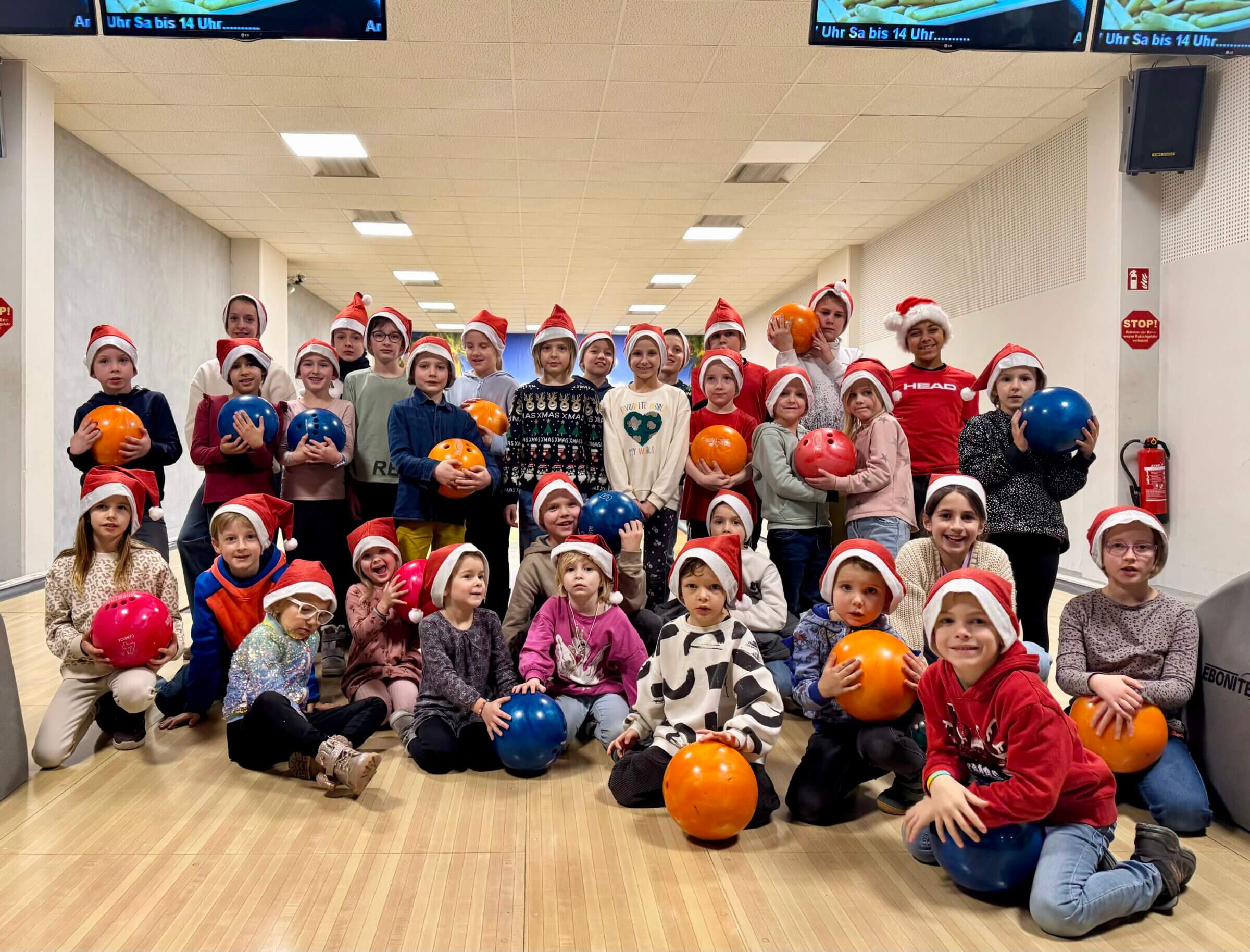 Kinder mit Weihnachtsmützen beim Bowling.