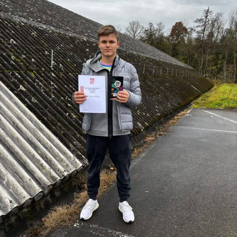 Junger Mann hält Urkunde und Pokal im Freien.